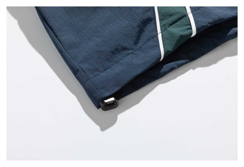 Close-up of the navy jacket hem with a dark green panel, white piping, and a small adjustment tab.