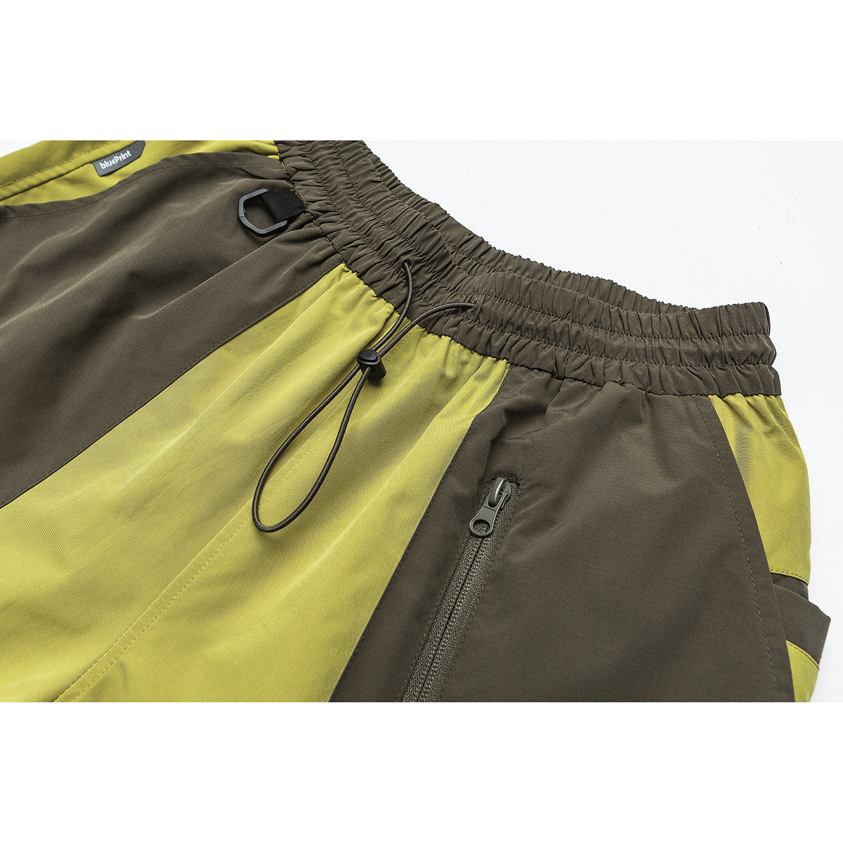Close-up of olive and chartreuse color-block shorts with an elastic waist, drawcord, clip loop and zip pocket.