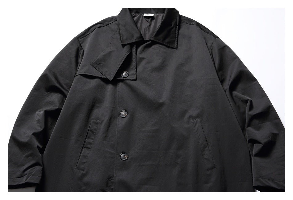 Upper front view of a black long coat with a wide collar, buttons, and slanted welt pockets.