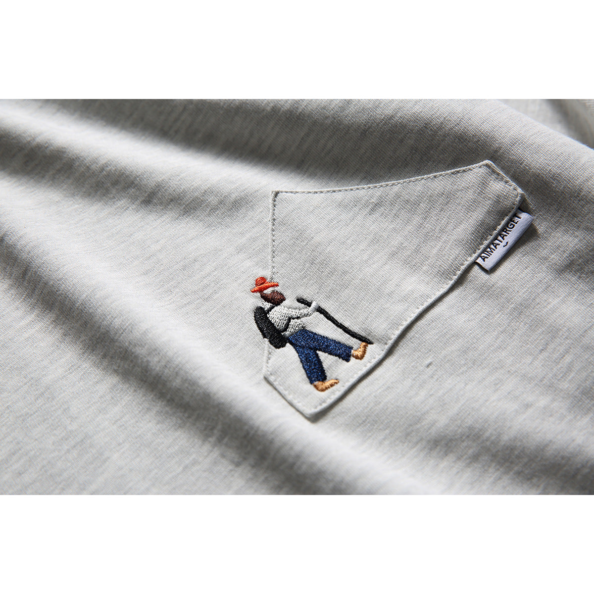 Close-up of a light gray shirt's chest pocket, showing an embroidered figure and a small sewn label.