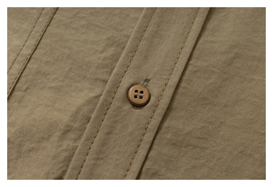 Close-up of a brown button on the stitched placket of a tan shirt.