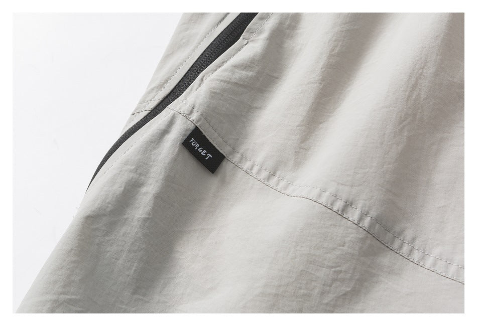 Close-up of light gray-beige pants with a black zipper and a small sewn black label.