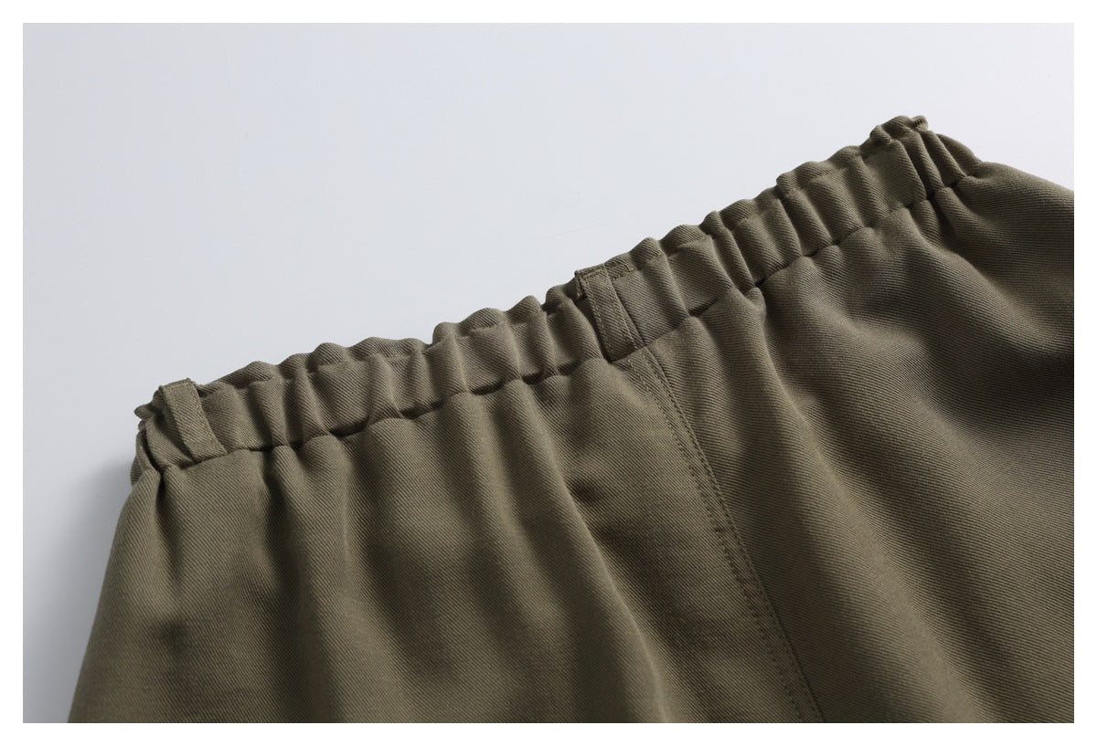 Close-up of olive-brown trousers showing the gathered waistband, belt loops and center back seam.