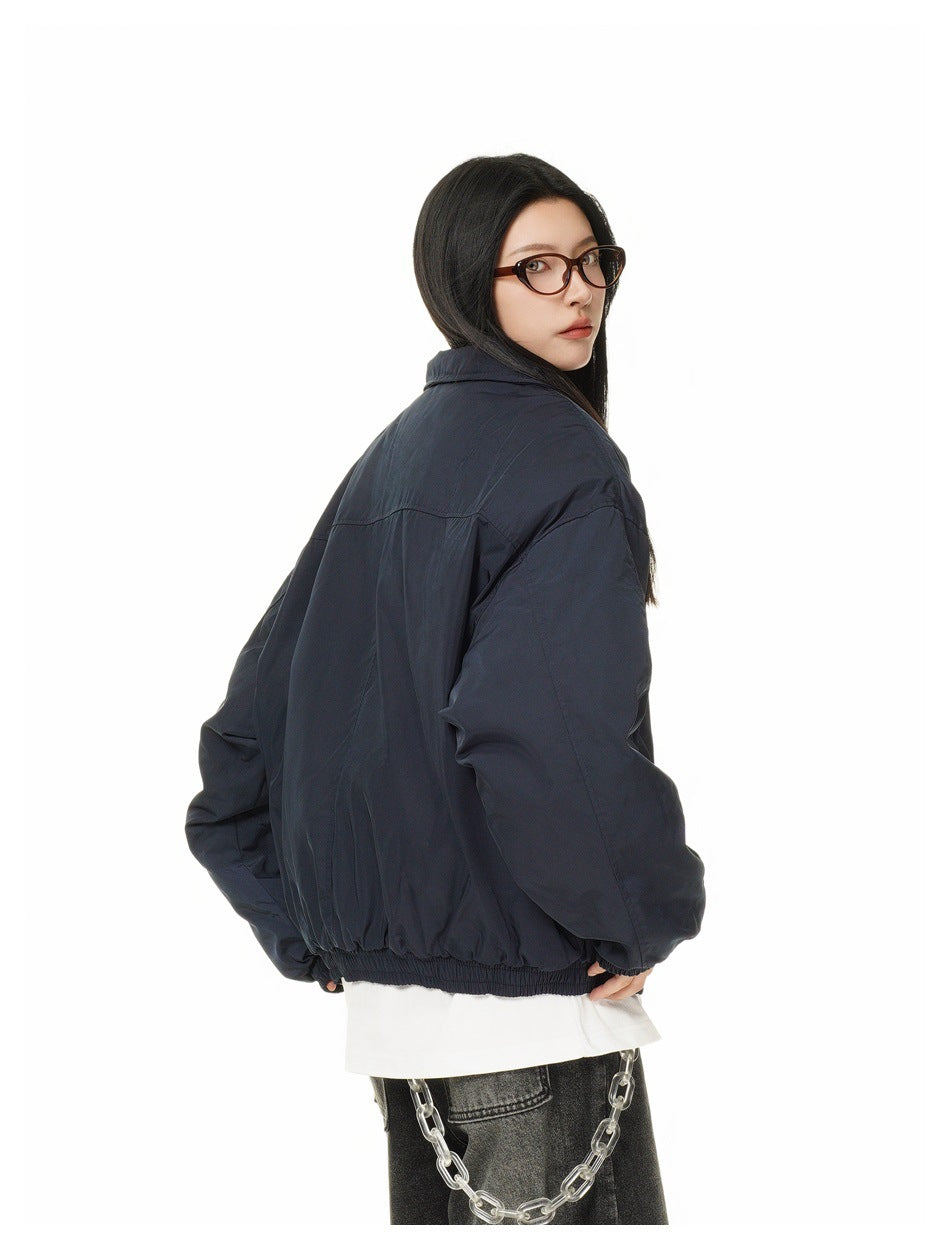 Model turned to show the back of an oversized dark navy jacket with a high collar and elastic hem.
