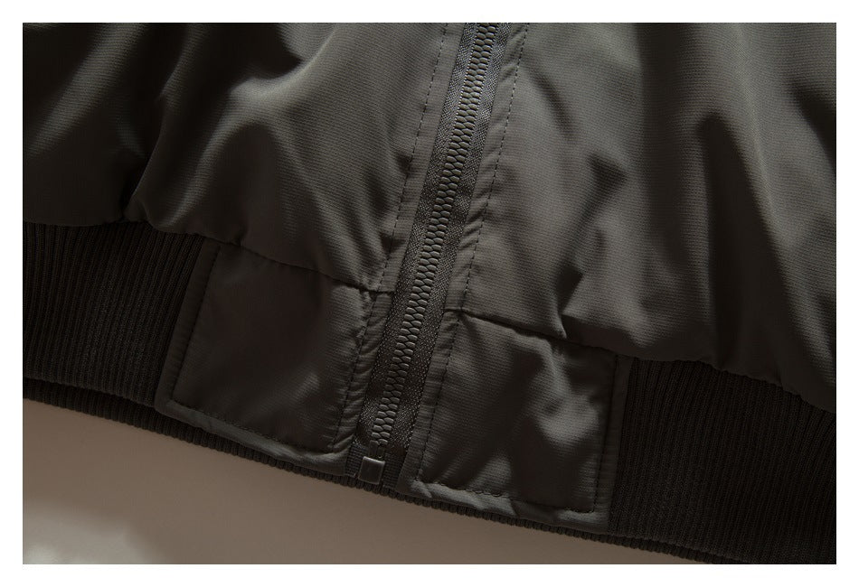 Close-up of the olive-gray jacket's front zipper, lower hem, and ribbed waistband.