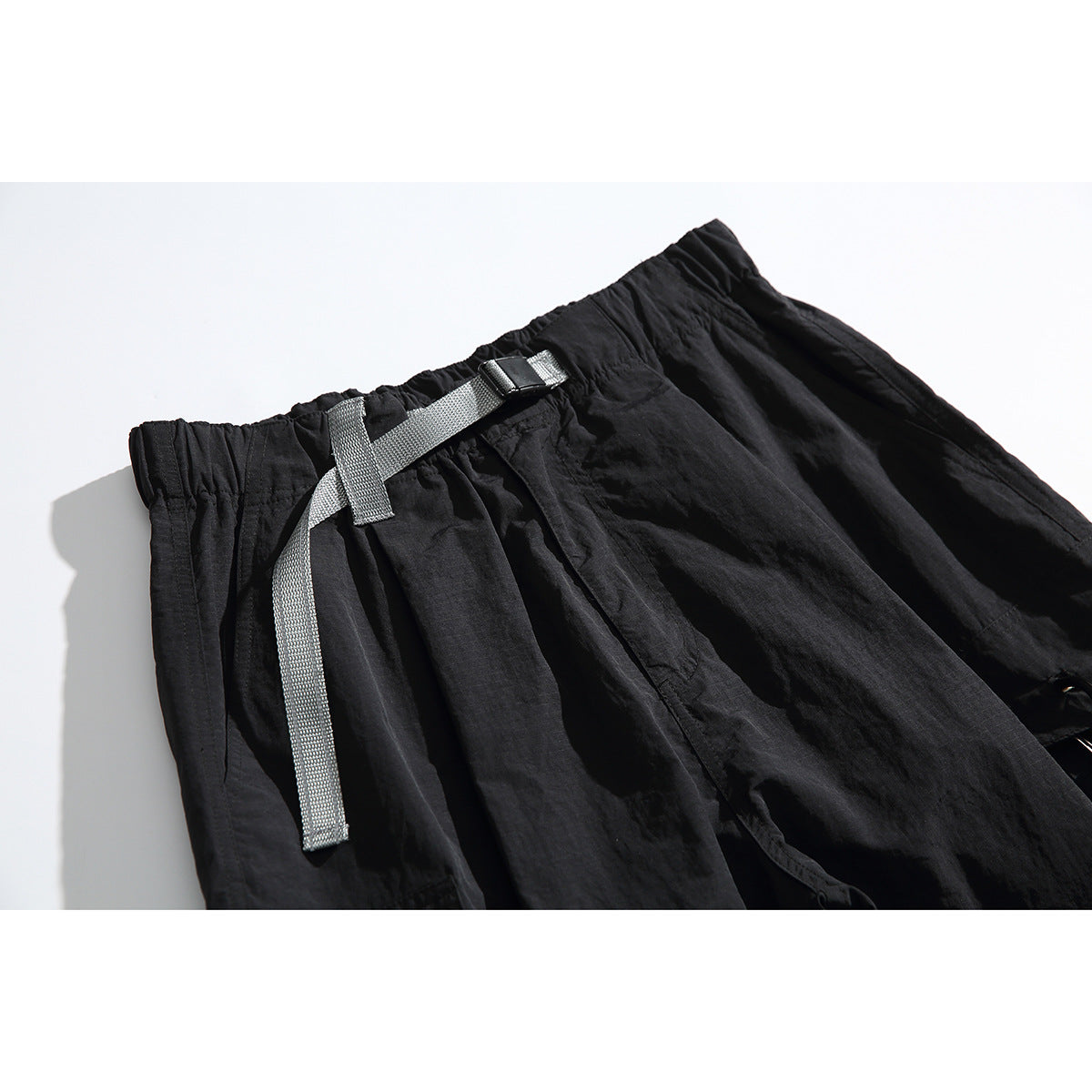 Close-up of black cargo trousers showing an elastic waistband and gray webbing belt with buckle.