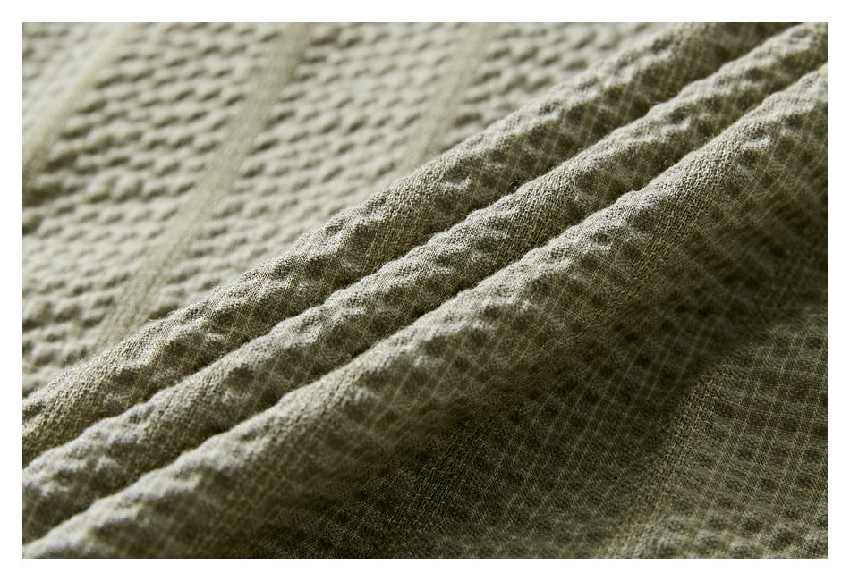 Macro view of the light olive shirt's raised, grid-like fabric texture and folded cloth.