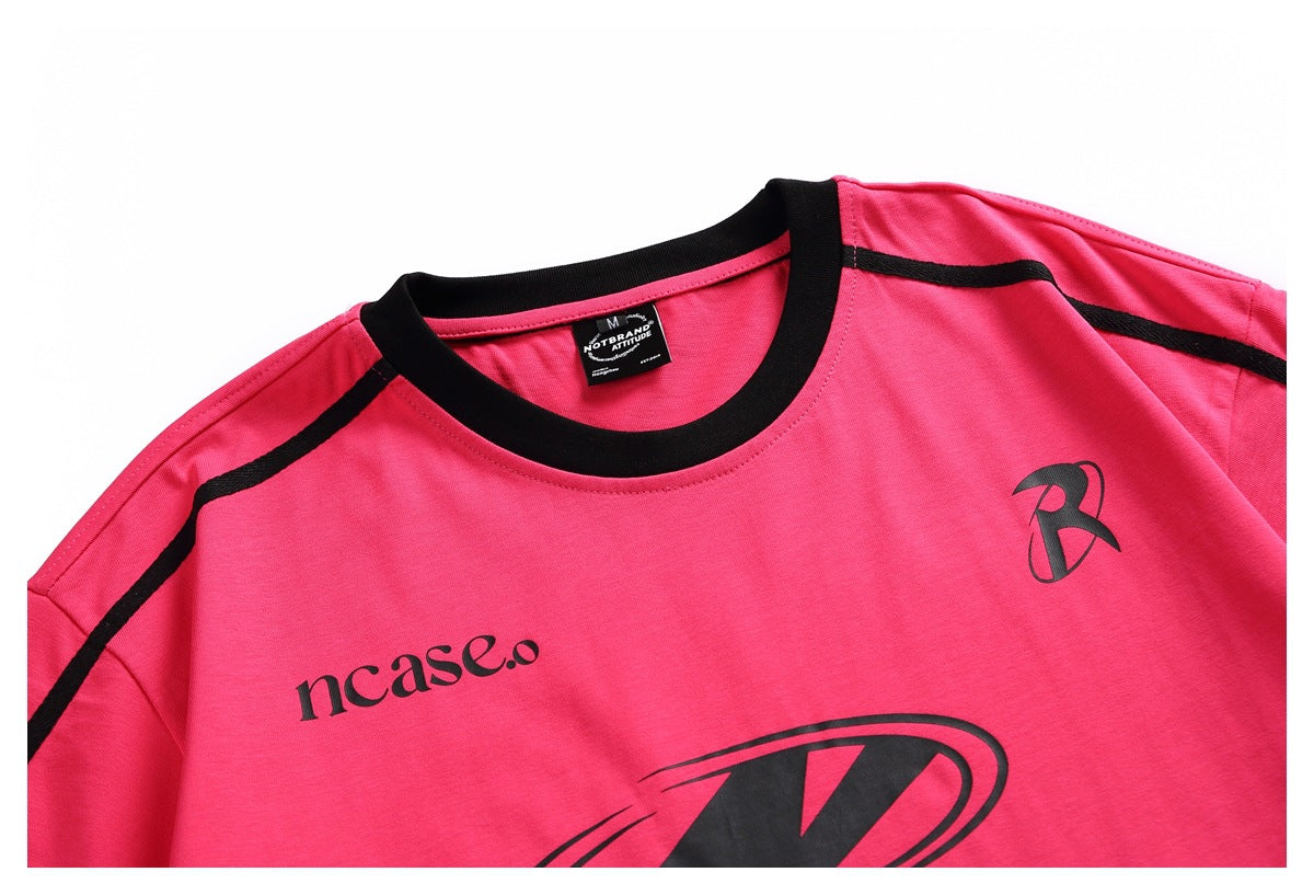 Close-up of a bright pink T-shirt with a black crew neck, shoulder piping, and black chest graphics.