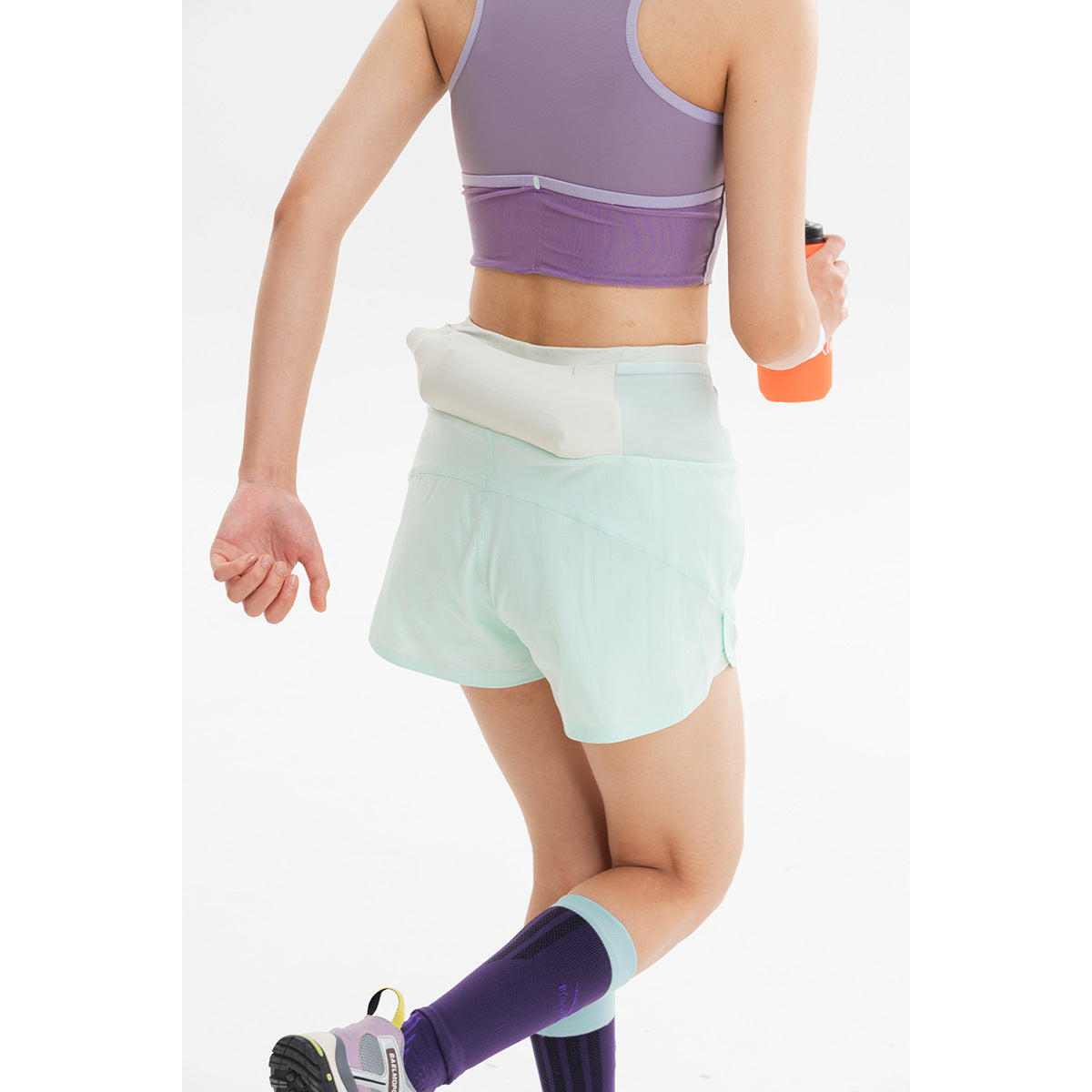 Rear view of a model wearing pale mint running shorts with a wide waistband and a purple cropped tank.