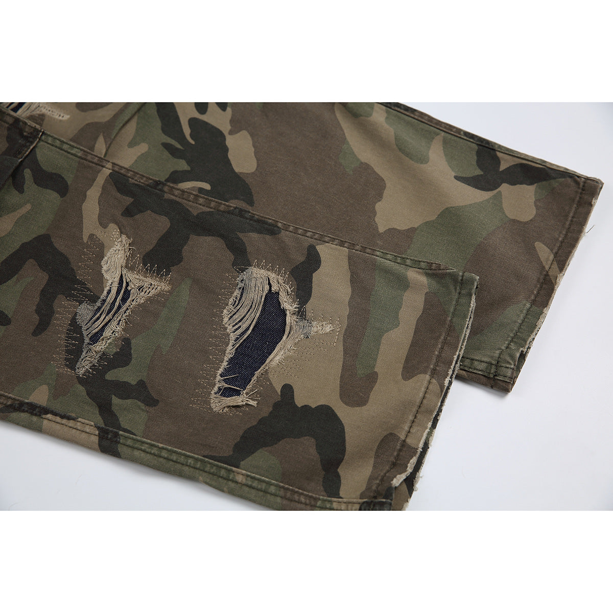 Close-up of distressed frayed openings on the leg of olive, brown and black camouflage trousers.