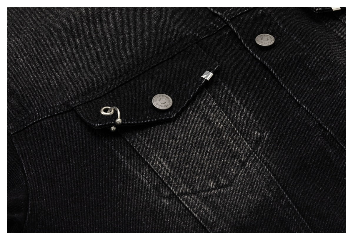 Close-up of a black denim jacket pocket flap with a metal button and silver hook detail.