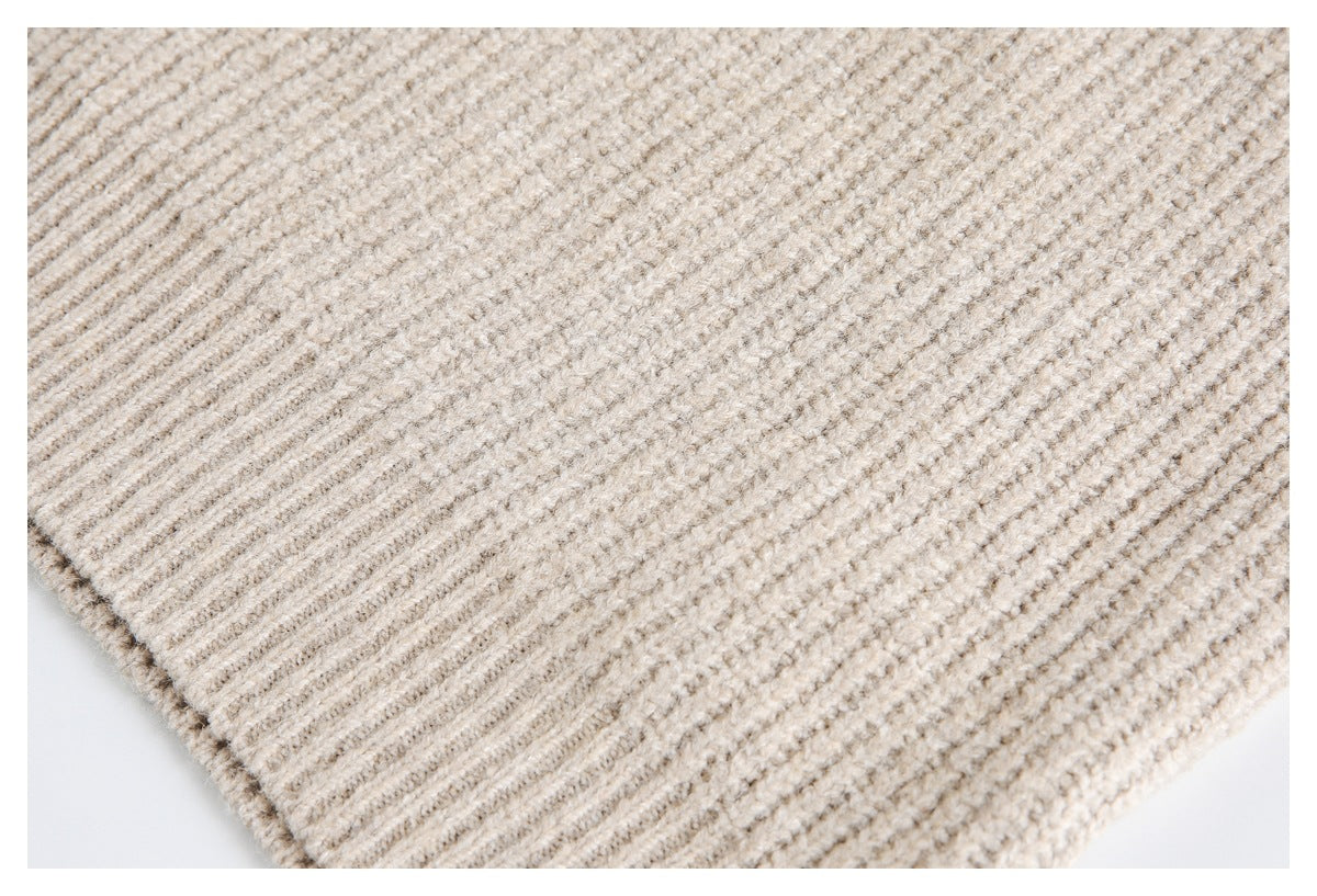 Close-up of a beige chunky knit garment with a ribbed edge and textured stitches.