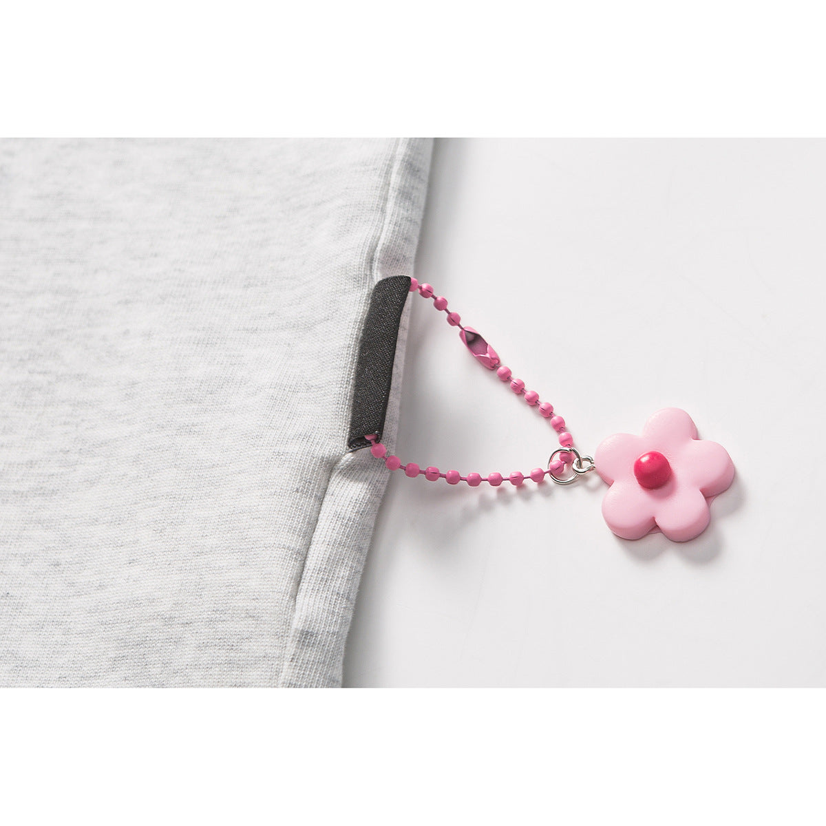 Close-up of a light gray T-shirt seam with a dangling pink beaded chain and flower charm.