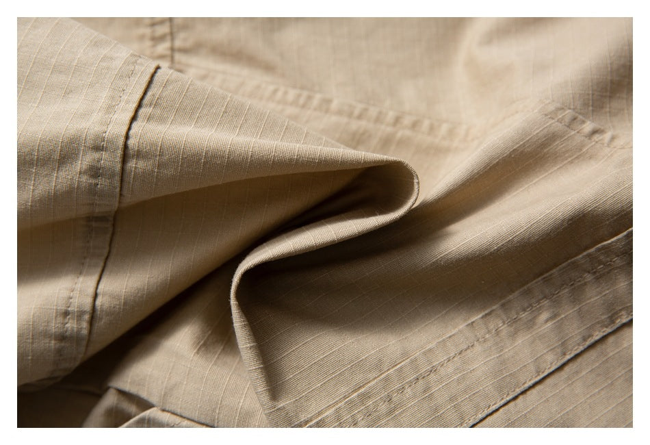 Close-up of folded tan trouser fabric showing the hem stitching and subtle horizontal texture.