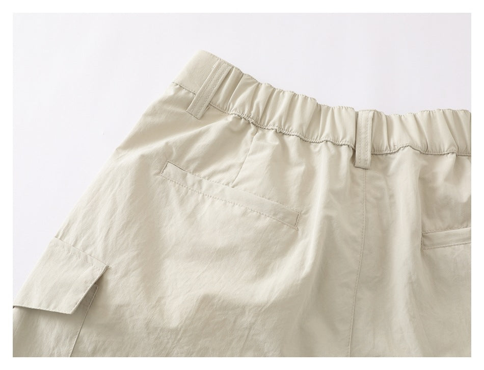 Back view of cream trousers showing a gathered waistband, belt loops, rear pockets, and a side cargo pocket.