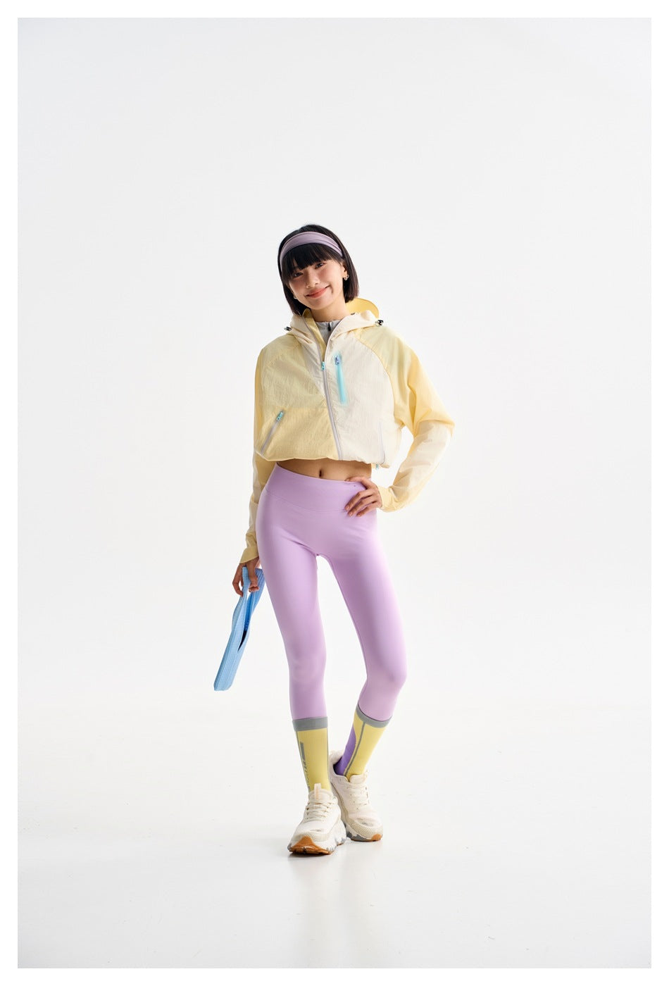 Model wearing a cropped pale yellow hooded jacket, lilac leggings, and yellow-and-purple color-block socks.