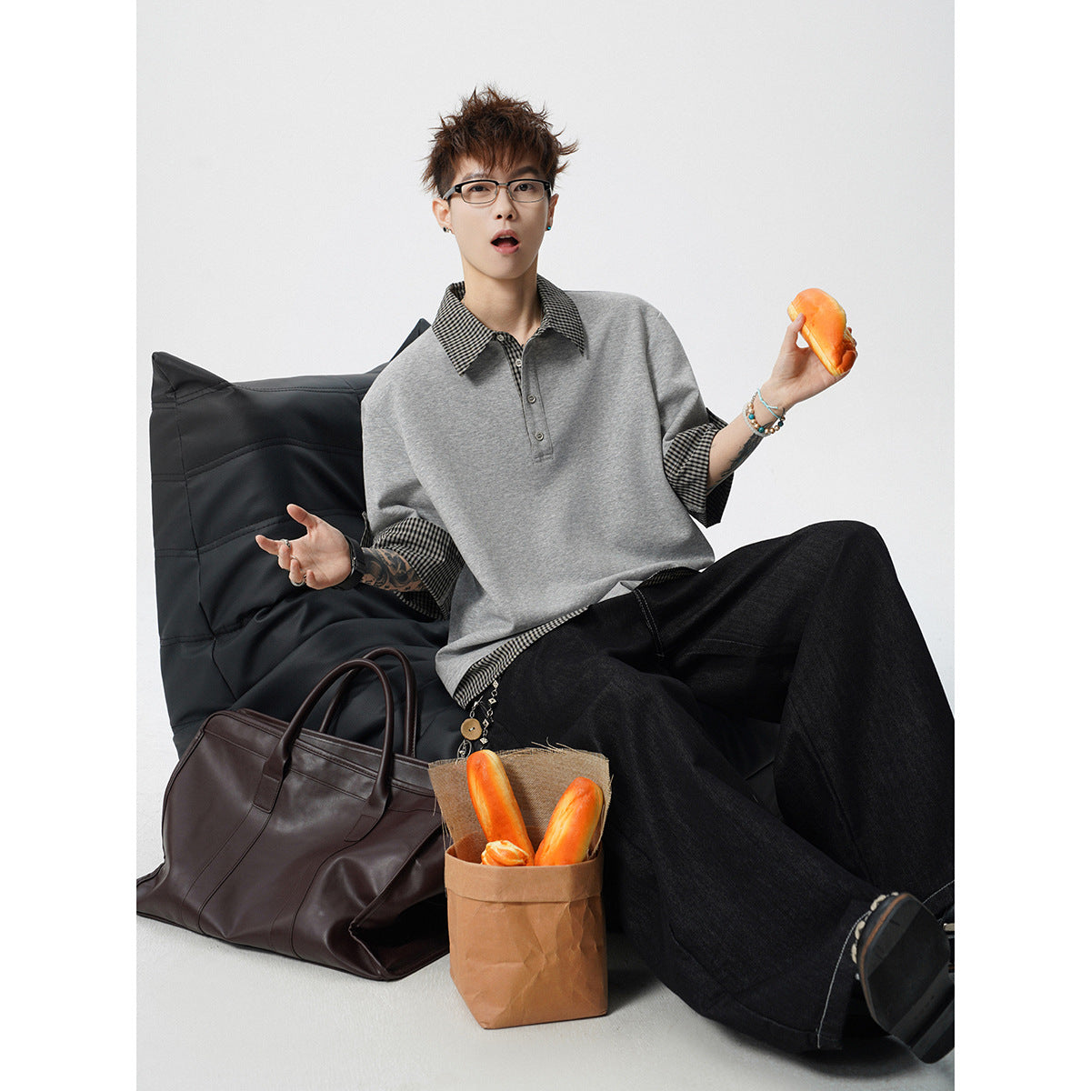 Seated model wearing a gray polo with checked collar, cuffs and hem, paired with dark wide-leg trousers.