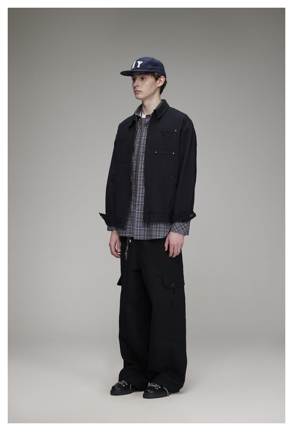 Full-length model wearing a black zip-front jacket with chest pockets over a plaid shirt and black cargo pants.