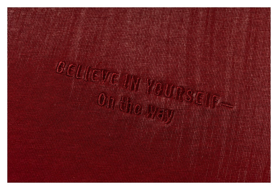Close-up of dark red embroidered English lettering on burgundy T-shirt fabric.