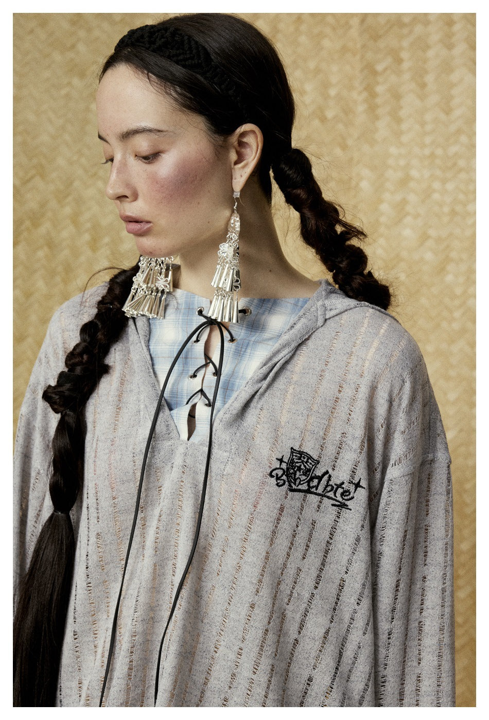 Close-up of a gray striped hooded top with black chest embroidery, lace-up neckline, and blue plaid inner layer.