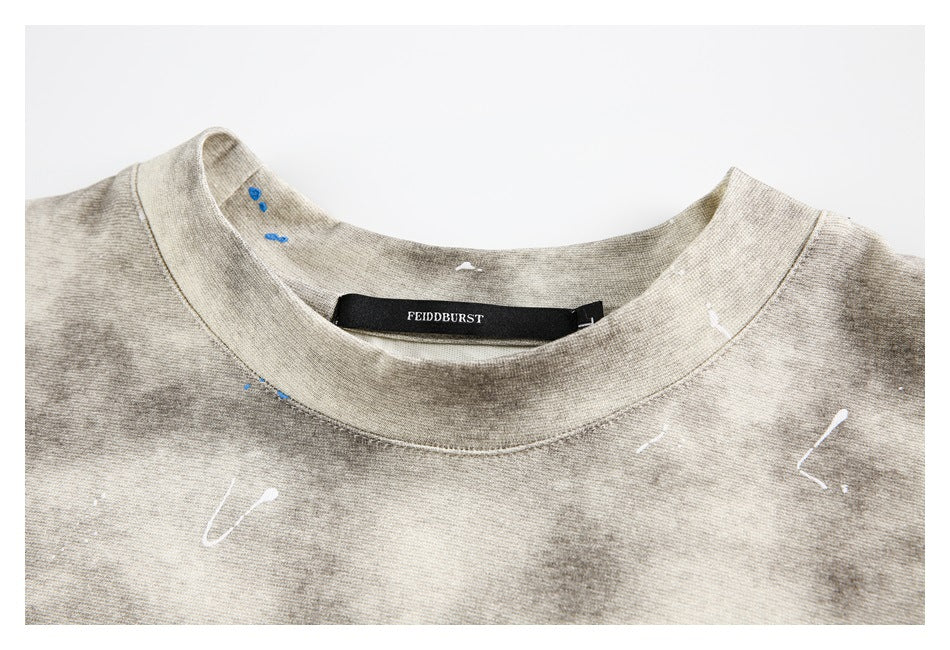 Close-up of a beige-gray T-shirt's ribbed crew neck, sewn-in black label, and scattered white and blue marks.