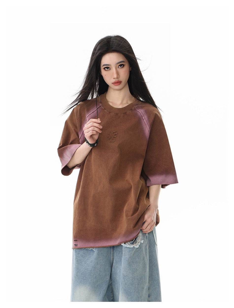 Front view of a model in an oversized brown T-shirt with mauve accents, raglan seams, and a raised chest emblem.