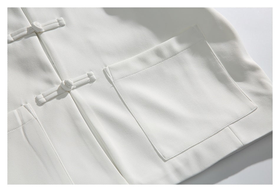Close-up of a large patch pocket and knotted frog closures on the white jacket.