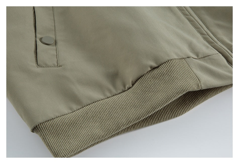 Close-up of an olive-gray jacket hem with ribbed trim, a snap tab, and part of a zipper.