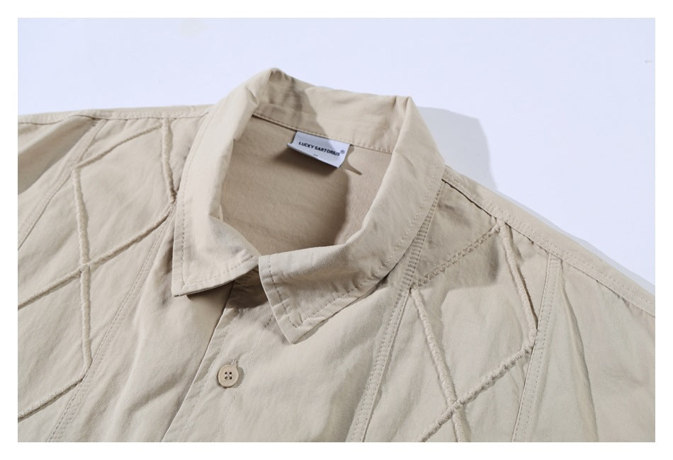 Close-up of a light beige shirt's collar, button, stitched panels, and sewn neck label.