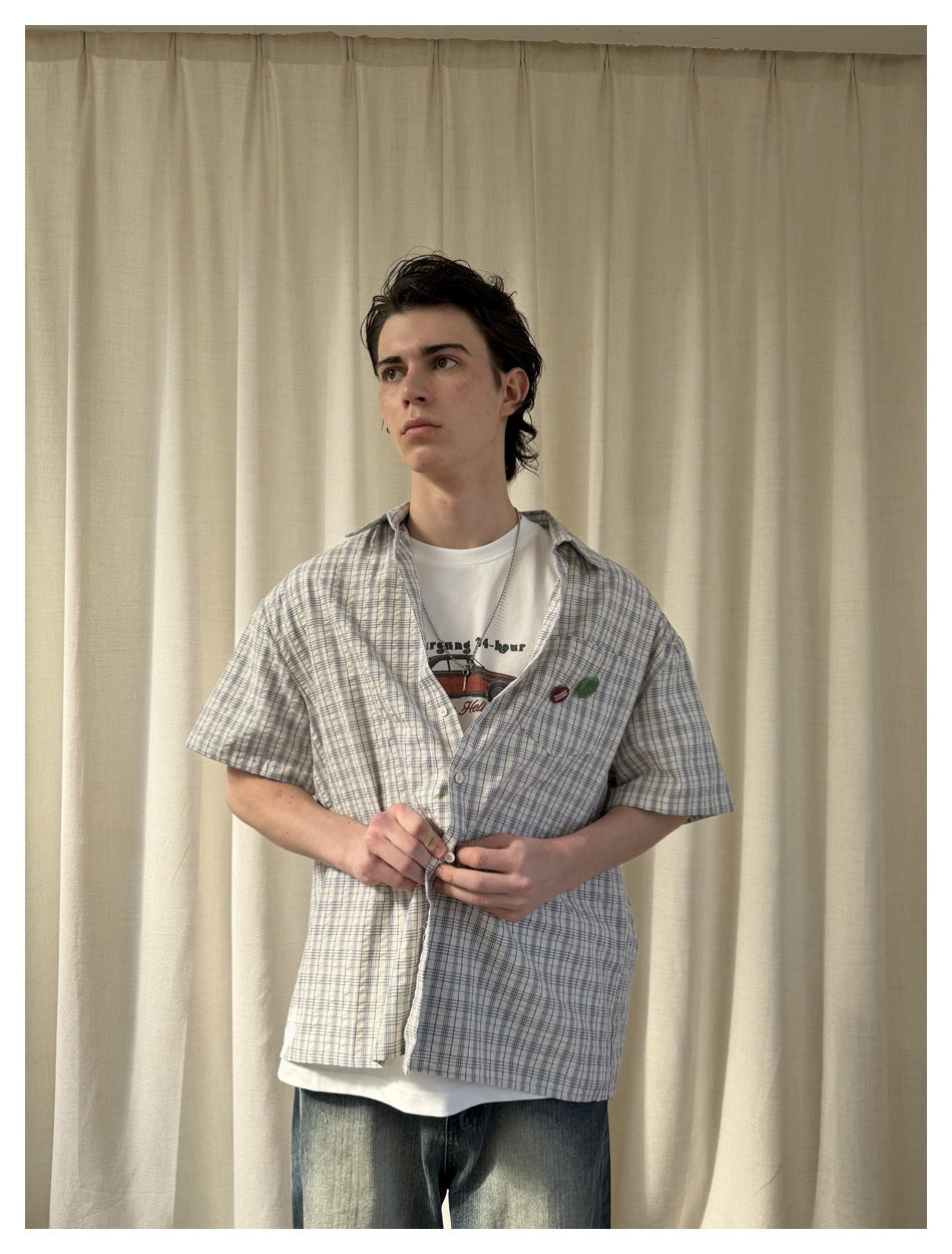 Model wearing a white and blue plaid short-sleeve button-up shirt over a white graphic tee and jeans.