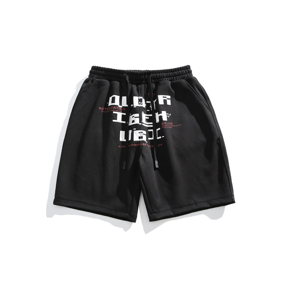 Black knee-length drawstring shorts with large white pixel-style lettering graphic on the front, flat lay