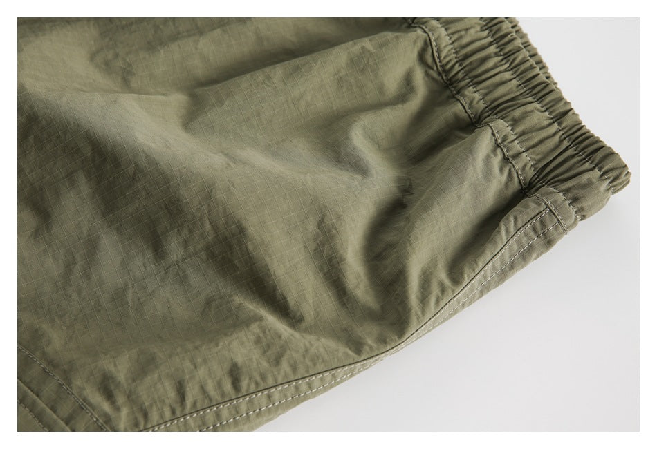 Close-up of olive shorts showing ripstop fabric texture, elastic waist edge and double-stitched hem.