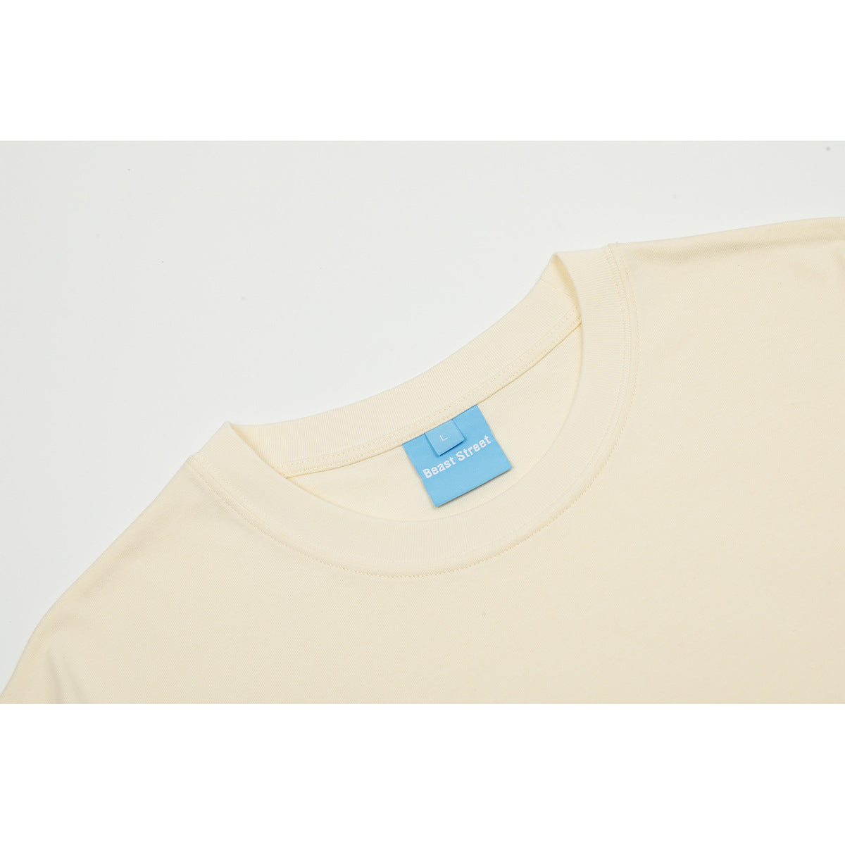 Close-up of a cream T-shirt crew neckline and blue Beast Street neck label.