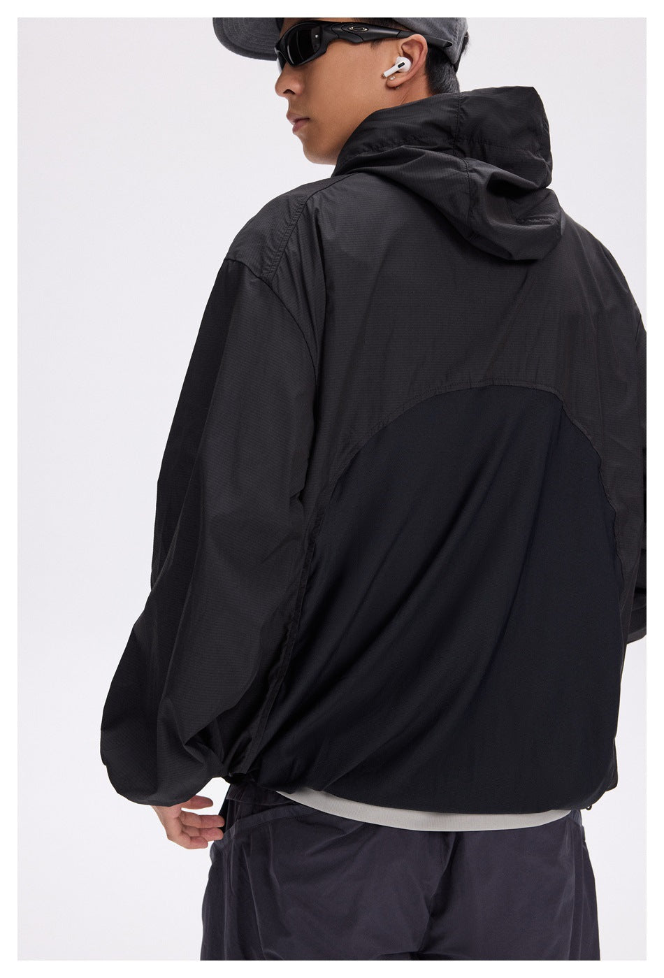Rear view of a model wearing a black hooded jacket with a large curved back panel.