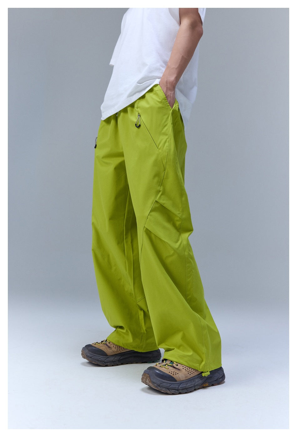 Side view of a model wearing loose lime-green pants with drawstring pocket details and hiking shoes.