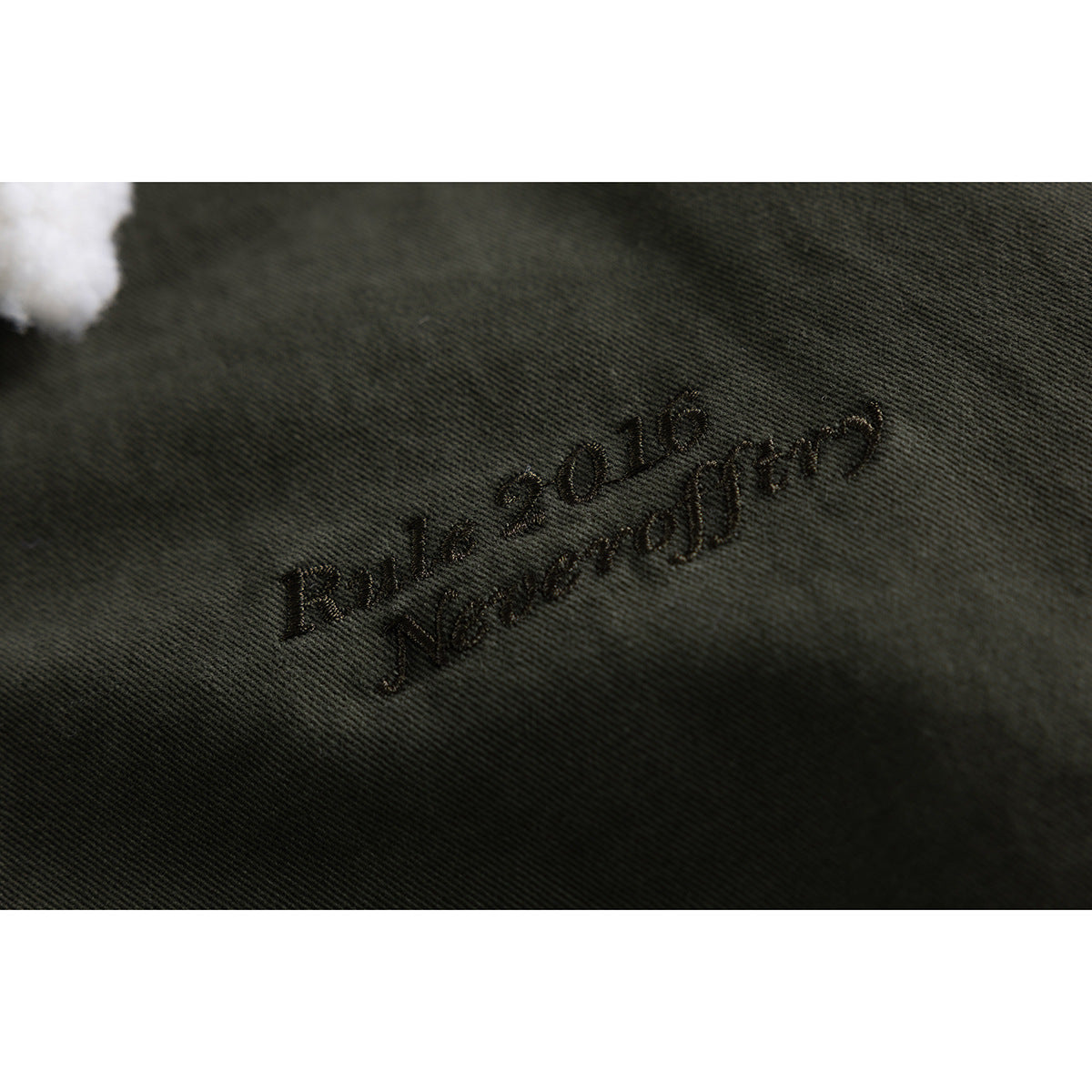 Close-up of dark embroidery on olive jacket fabric beside a small edge of the white collar.