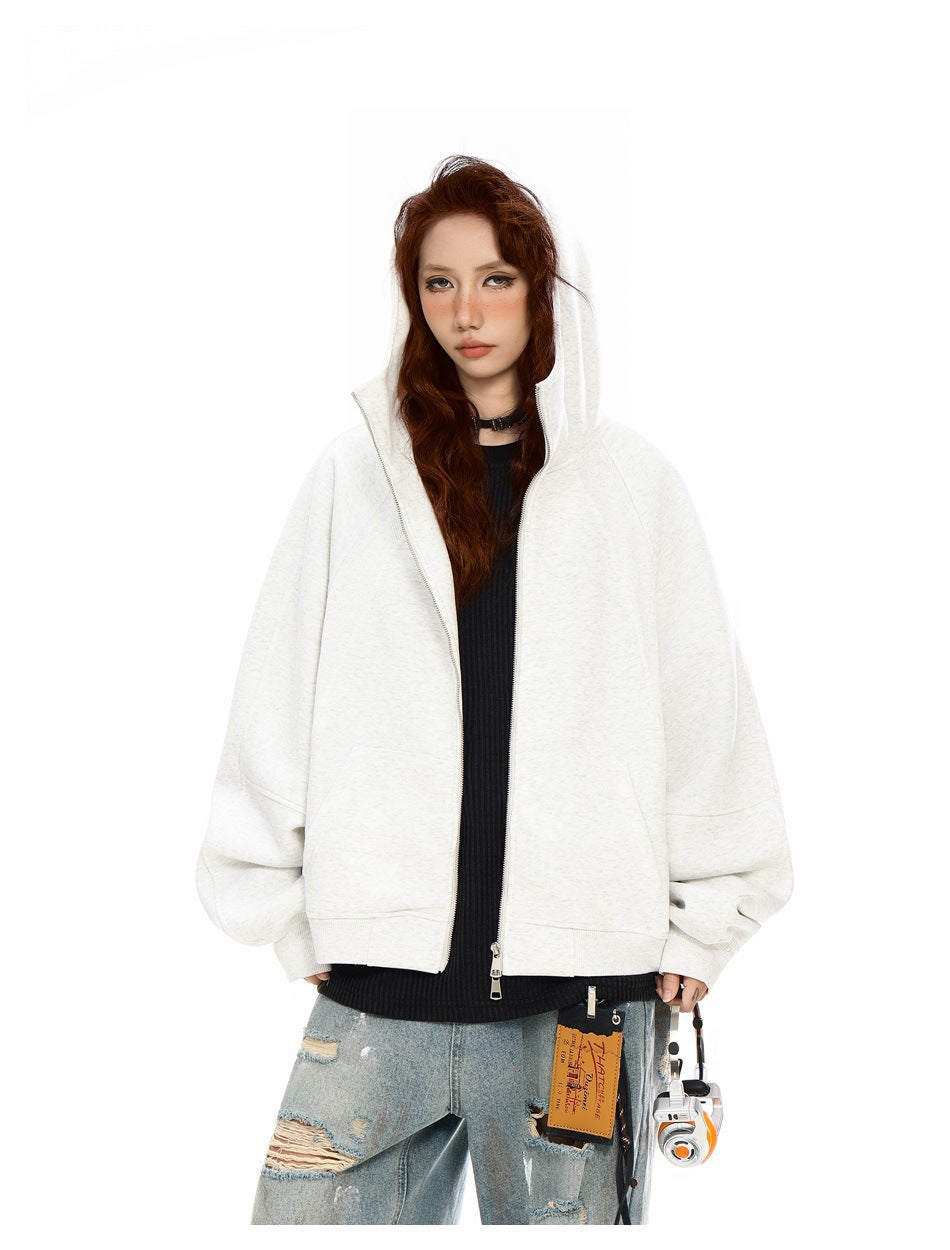 Model wearing a light gray oversized zip hoodie with the hood up, open over a black top and distressed jeans.