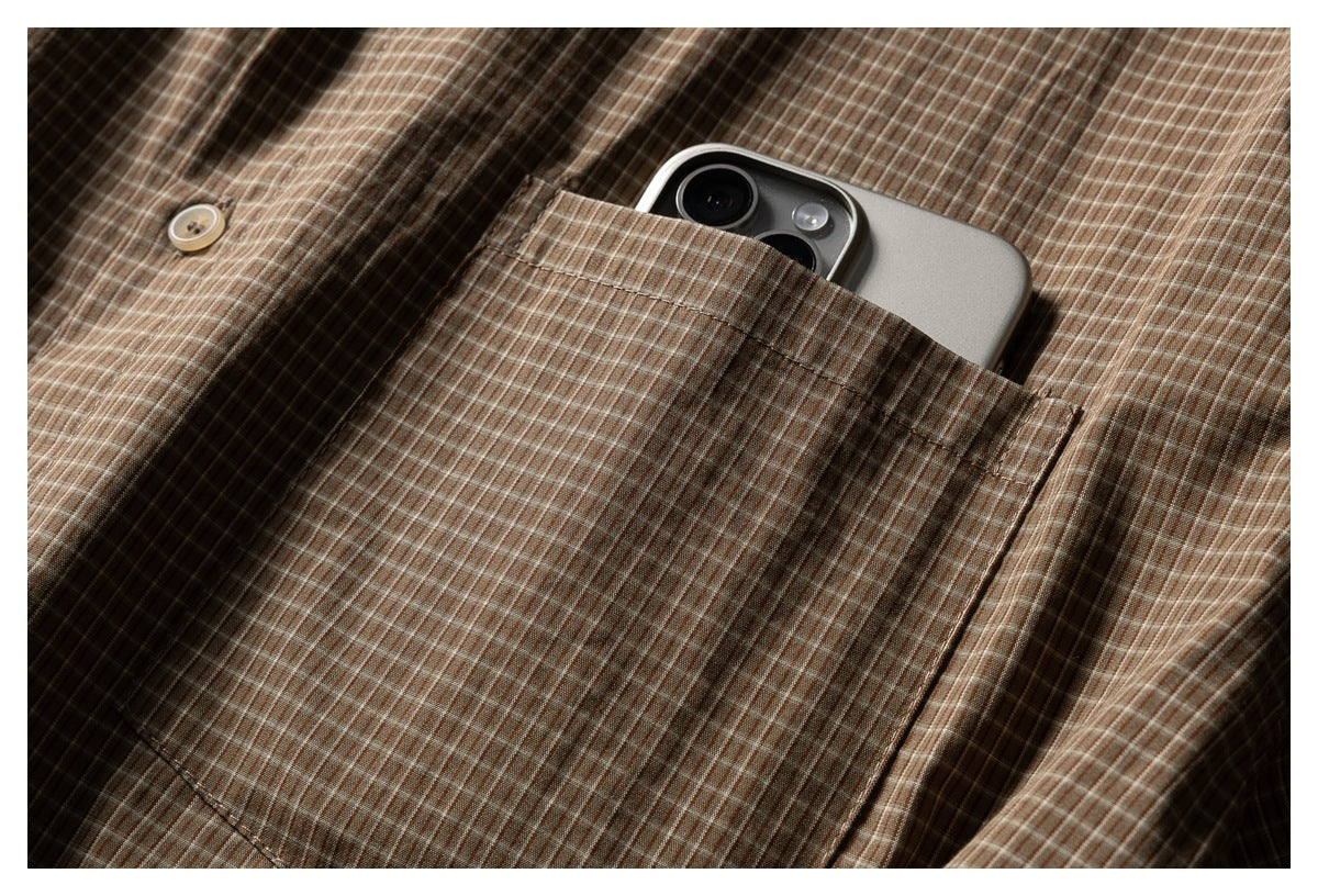 Close-up of the shirt's brown checked chest pocket holding a smartphone.