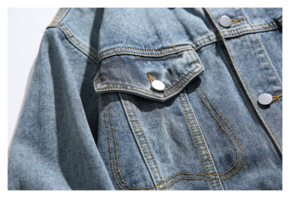 Close-up of a flap chest pocket and double-stitched seams on a faded blue denim jacket.