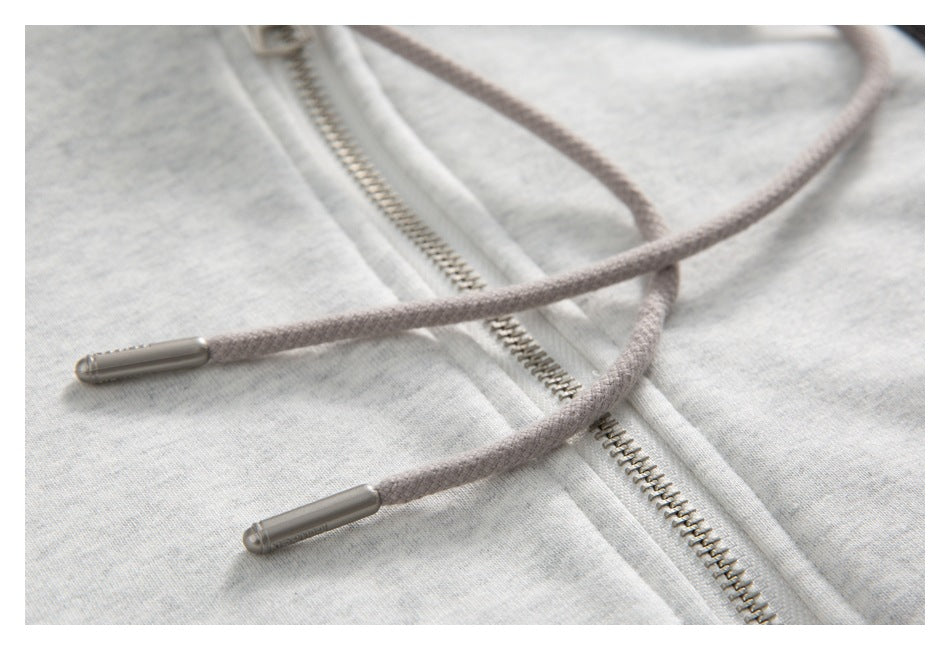 Close-up of gray drawstrings with metal tips crossing over a metal zipper on light gray fabric.