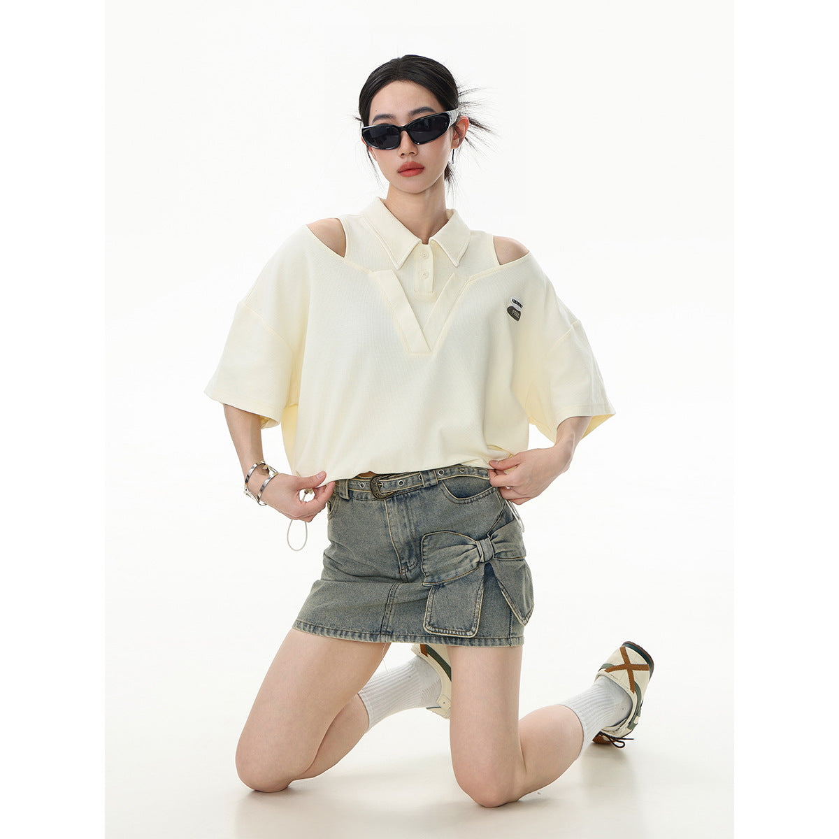 Model wearing an ivory cutout-shoulder polo with a gray denim mini skirt.