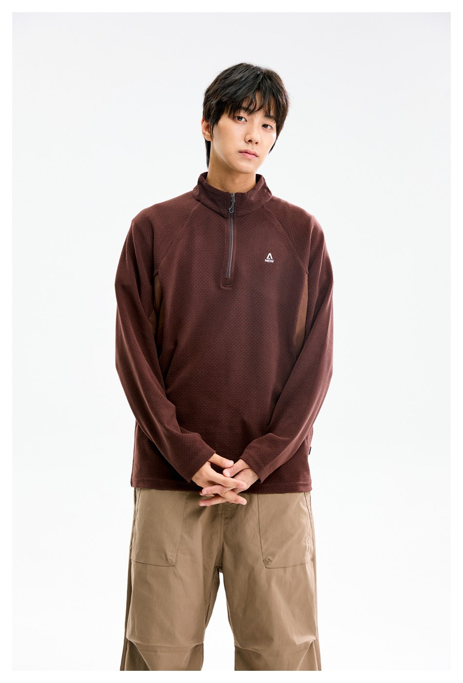 Model wearing a burgundy quarter-zip pullover with a stand collar, front view, hands clasped.