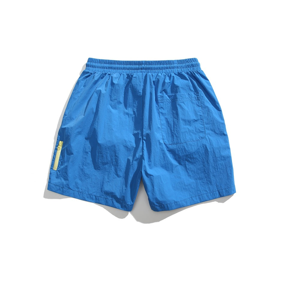 Back view of bright blue shorts with an elastic waistband, rear patch pocket, and yellow zip detail on the left leg.