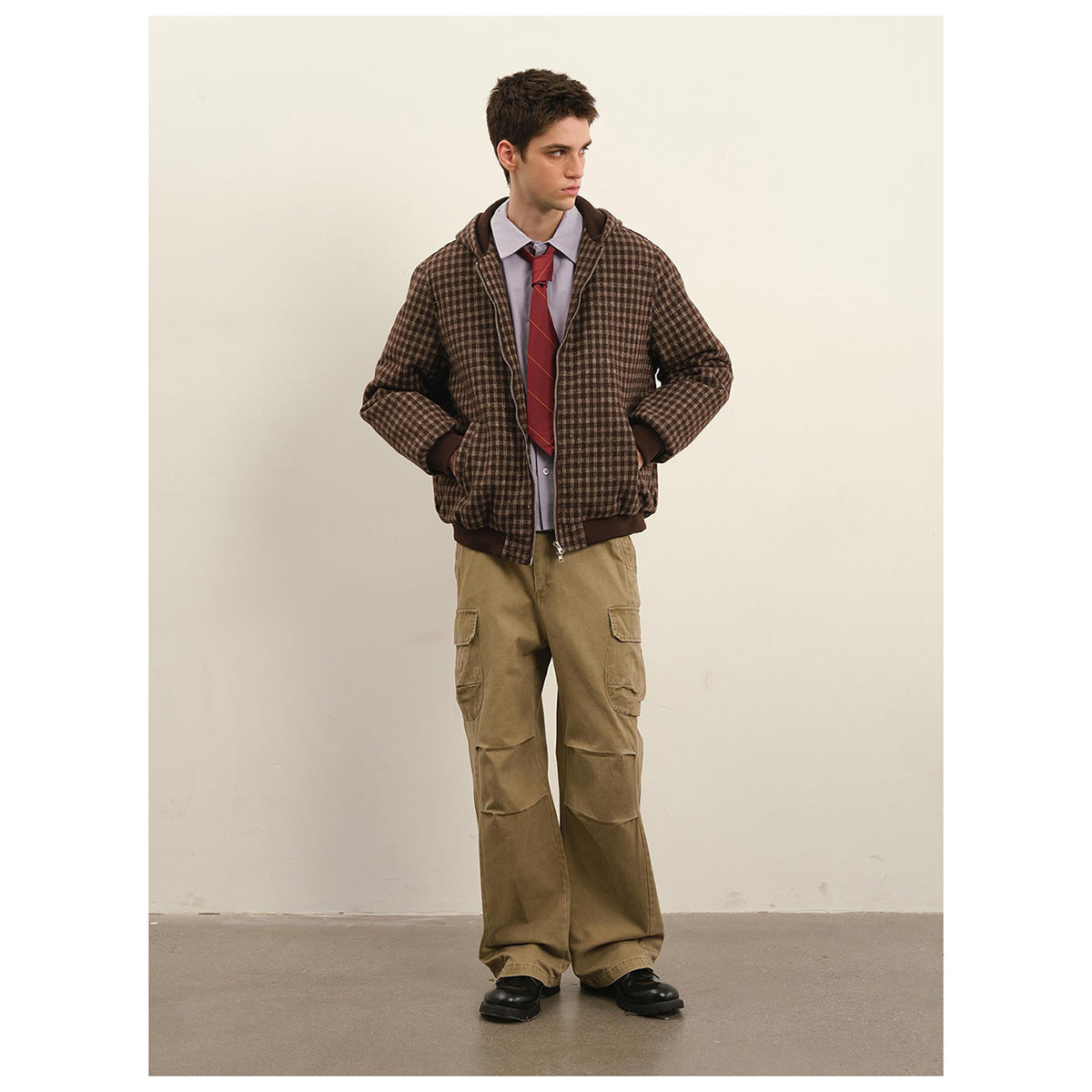 Model wearing a brown check hooded zip jacket with dark ribbed trim, shown with tan cargo pants.