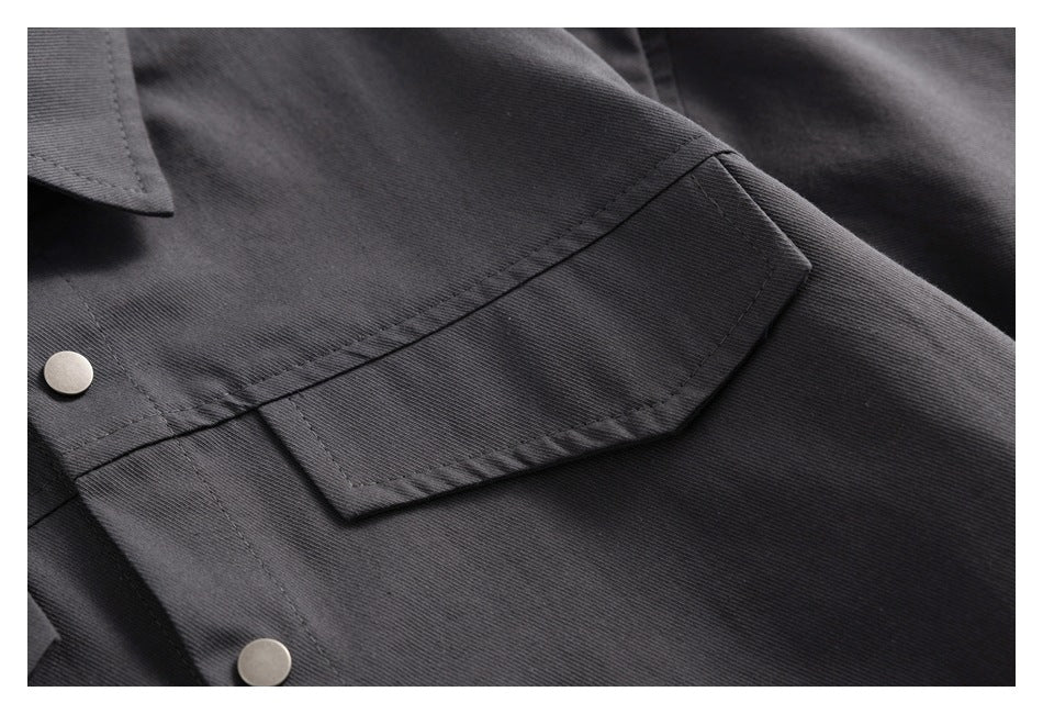 Close-up of a dark charcoal shirt pocket flap with visible stitching and metal snap buttons.