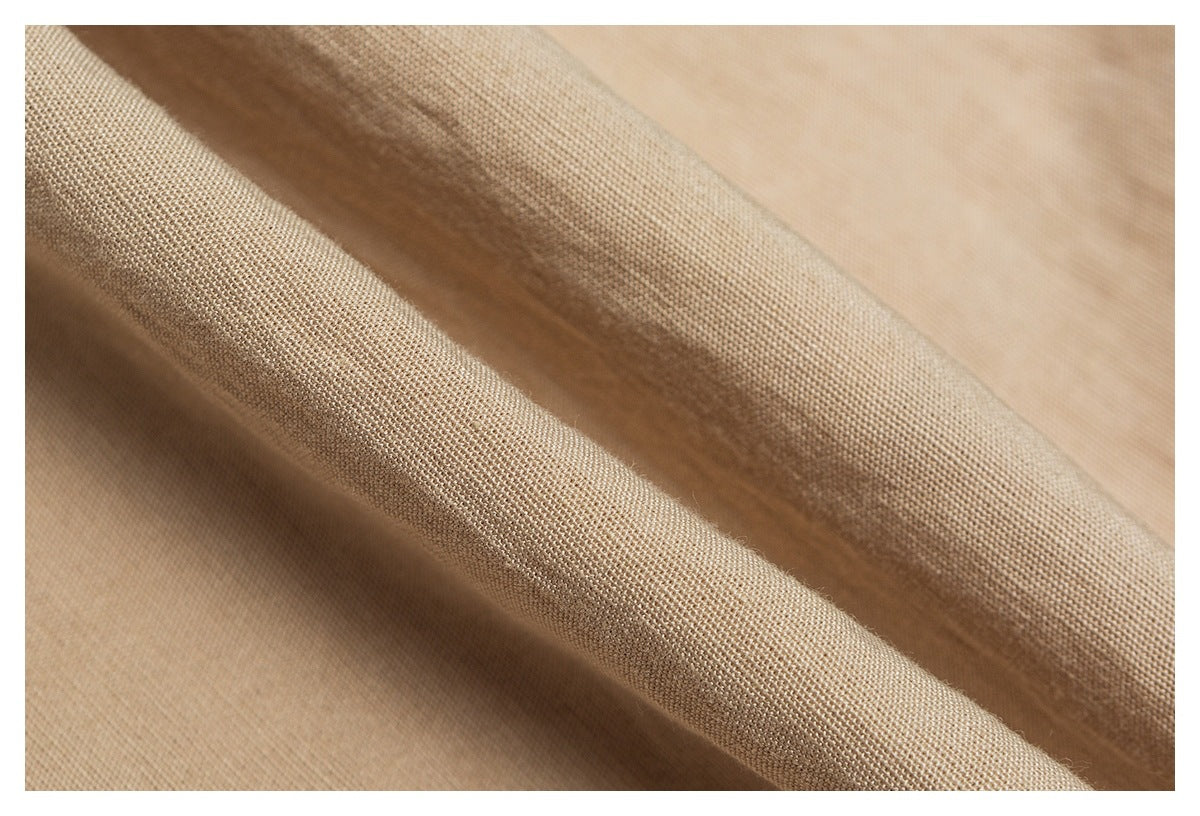 Macro view of tan trouser fabric draped into folds, showing its woven texture.