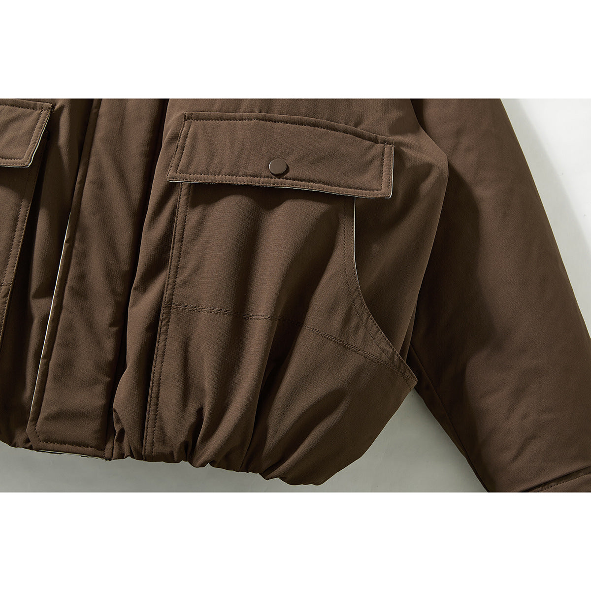 Close-up of a brown jacket's flap pocket with snap button and large lower pocket.