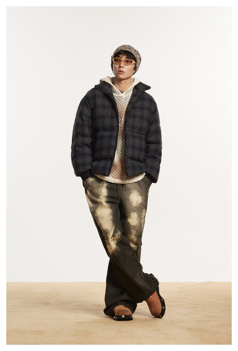 Model wearing the plaid puffer jacket zipped over a cream knit top, with wide dark washed pants and a beanie