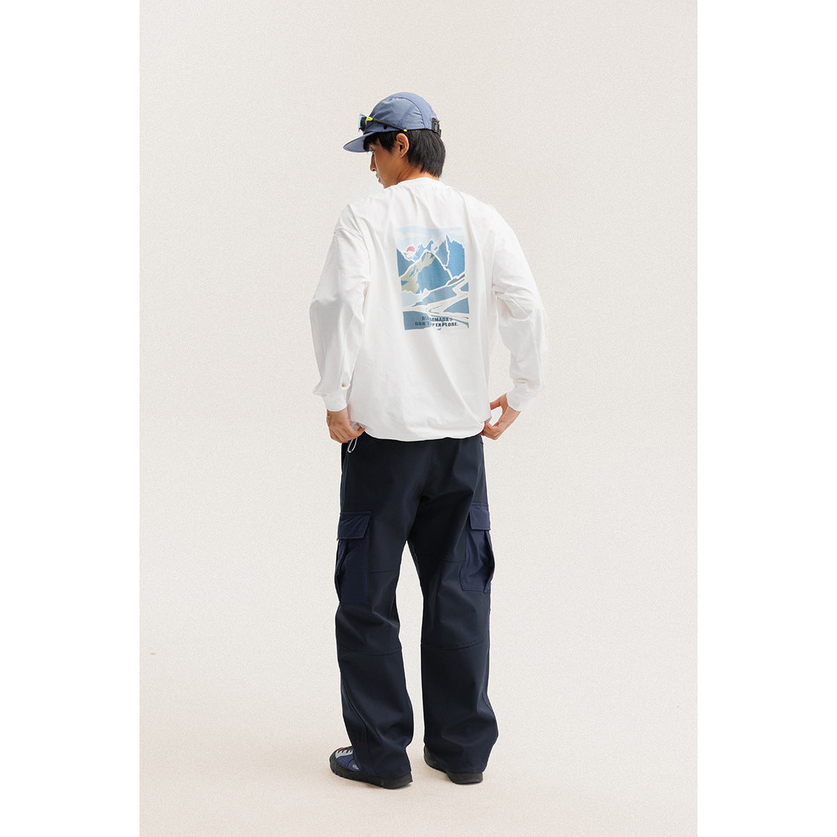Back view of a model in a white long-sleeve shirt with a mountain graphic and navy cargo pants.