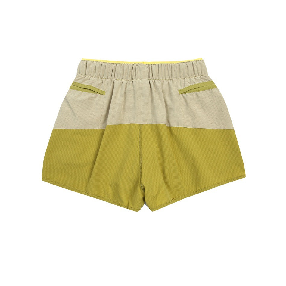 Back view of color-block athletic shorts in beige and yellow-green with an elastic waistband and angled pocket openings.